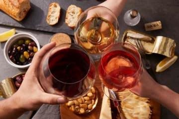 Drei Personen stoßen mit je einem Glas Weiß-, Rot- und Rosewein an