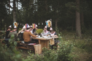 Schweden sitzen im Wald an einem Holztisch und feiern das Krebsfest