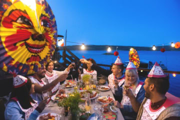 Menschen feiern eine traditionelle Kräftskiva mit Krebsen, Papierhüten und Lampions an einer festlich gedeckten Tafel in Schweden.