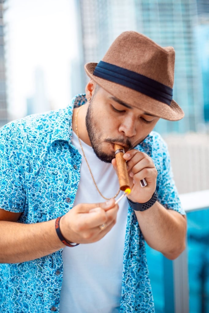 Latino mit Hut zündet sich Zigarre an