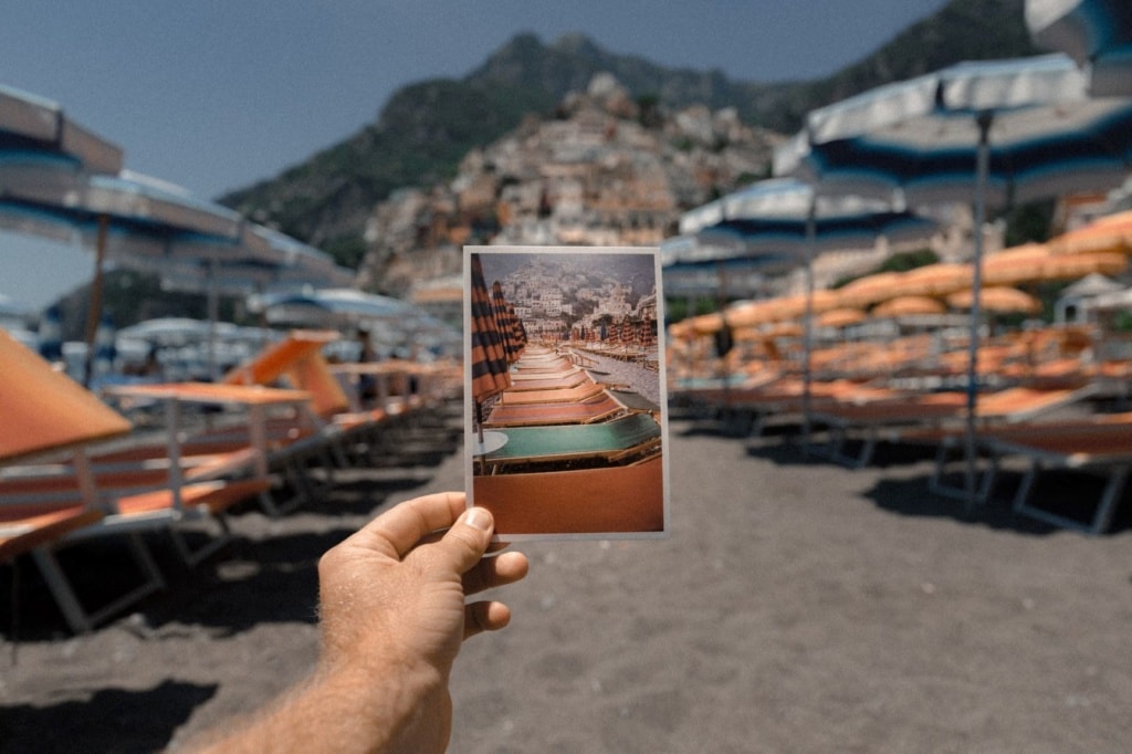 App-Tipps für die Reise: Mann hält am Strand eine Postkarte in die Kamera