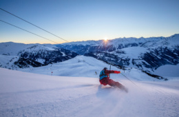 Ski-Fahrer auf der Winterskipiste in Österreich. Farbiger Sonnenaufgang im Hintergrund.