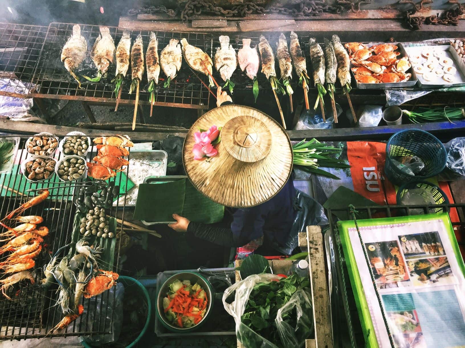 Ein Koch auf einem Nachtmarkt in Bangkok grillt mehrere Fische gleichzeitig.