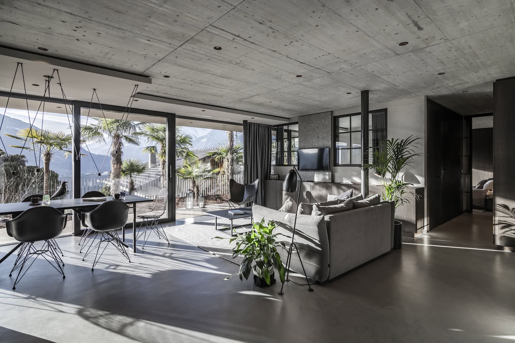 Wohnbereich im Apartment 7 in Schenna mit Sichtbeton, Loft-Charakter und Terrasse mit Palmen