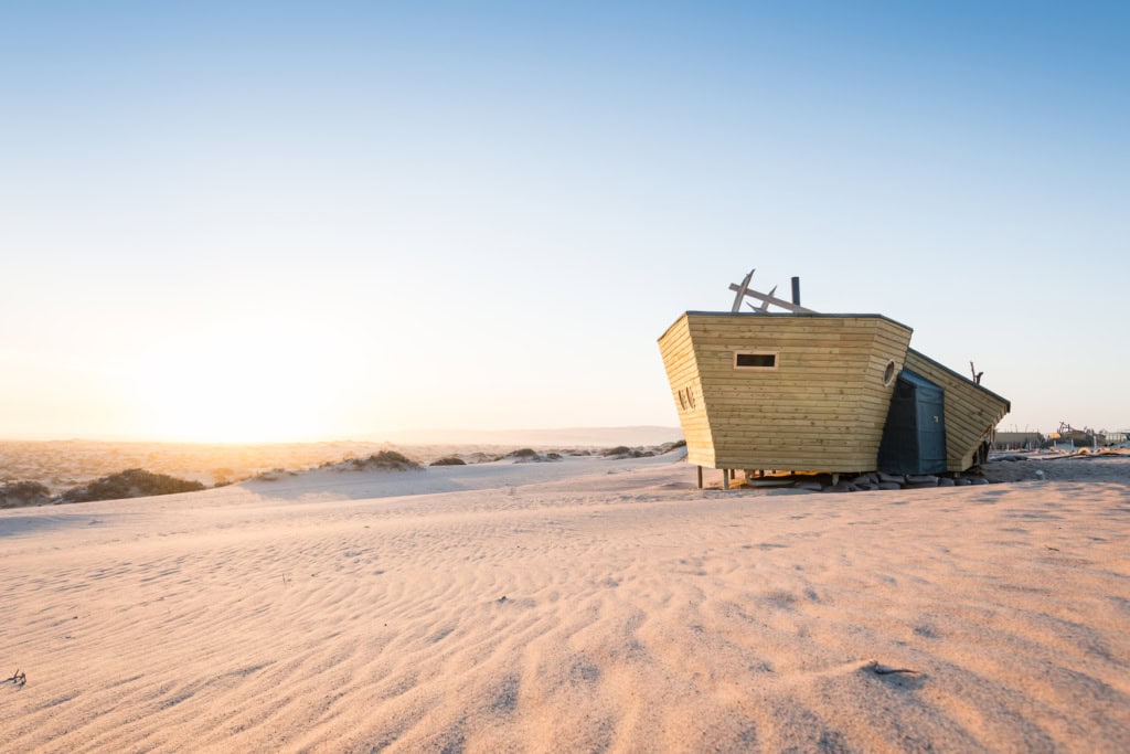 Schiffsförmige Holzhütte der Shipwreck Lodge in den Dünen der Skelettküste im Abendlicht