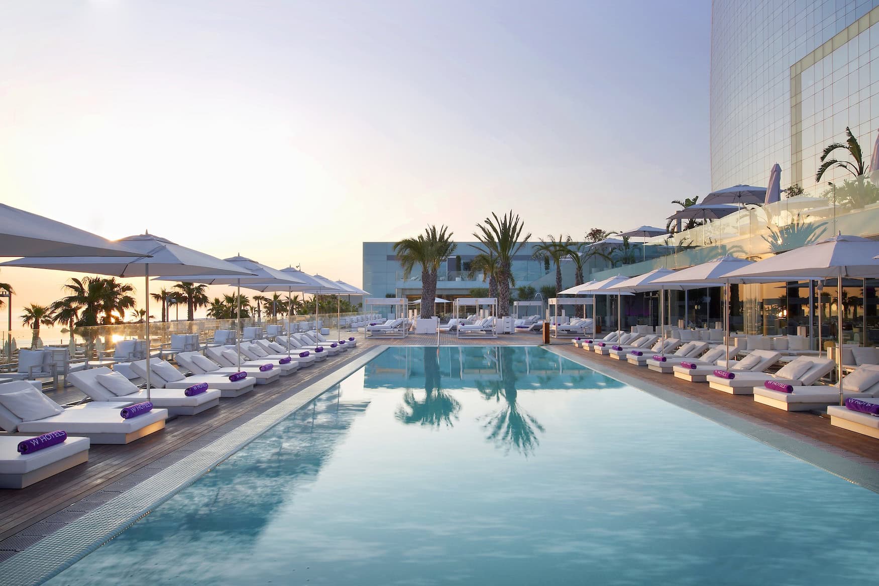 Poolbereich des W Barcelona mit weißen Liegen und Palmen im Abendlicht