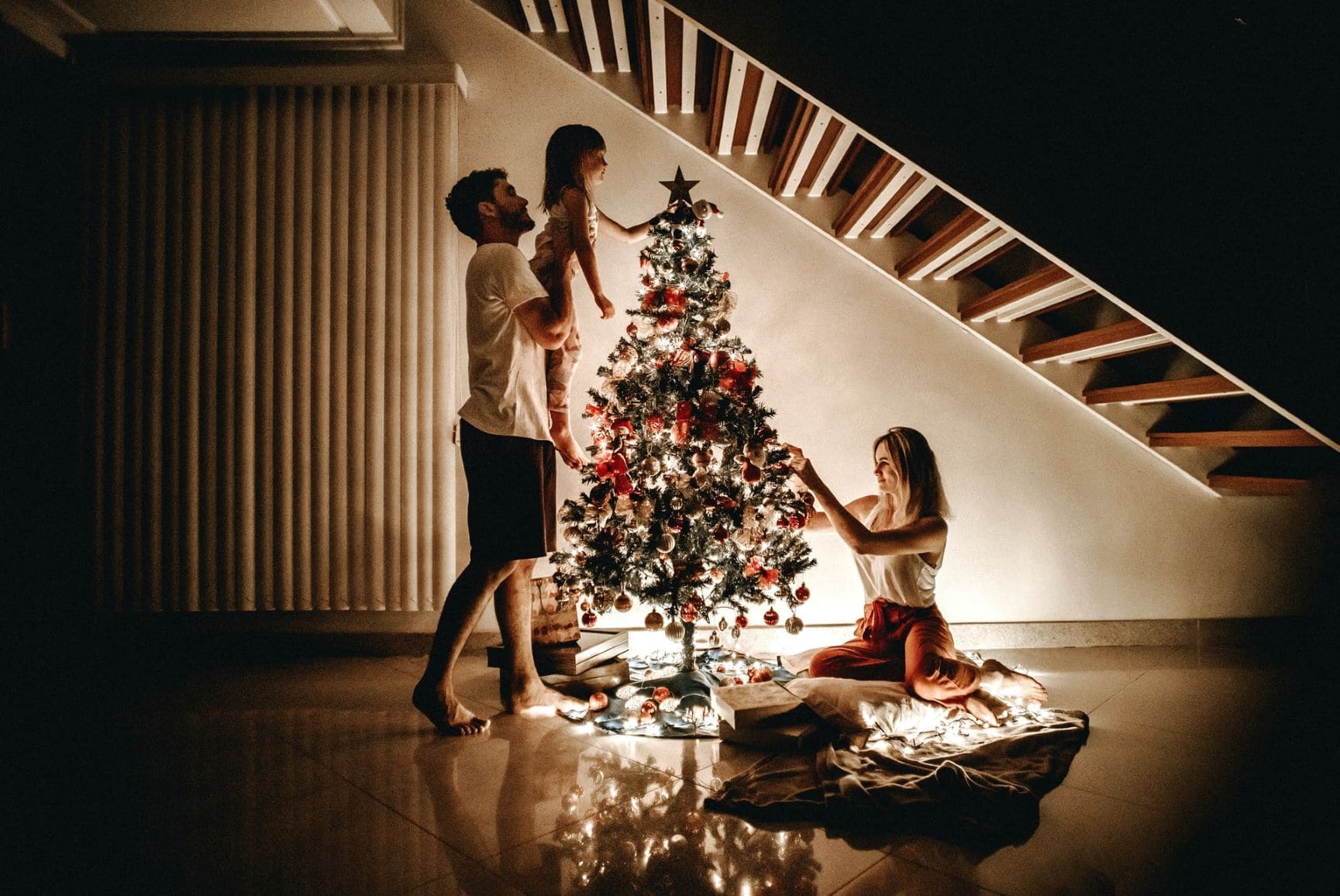 Mann, Frau und Kind schmücken Weihnachtsbaum unter Treppe