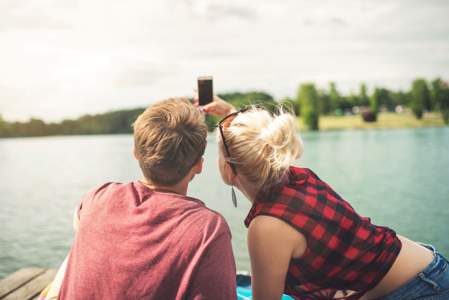Junger Mann und junge Frau machen am Wasser ein Selfie
