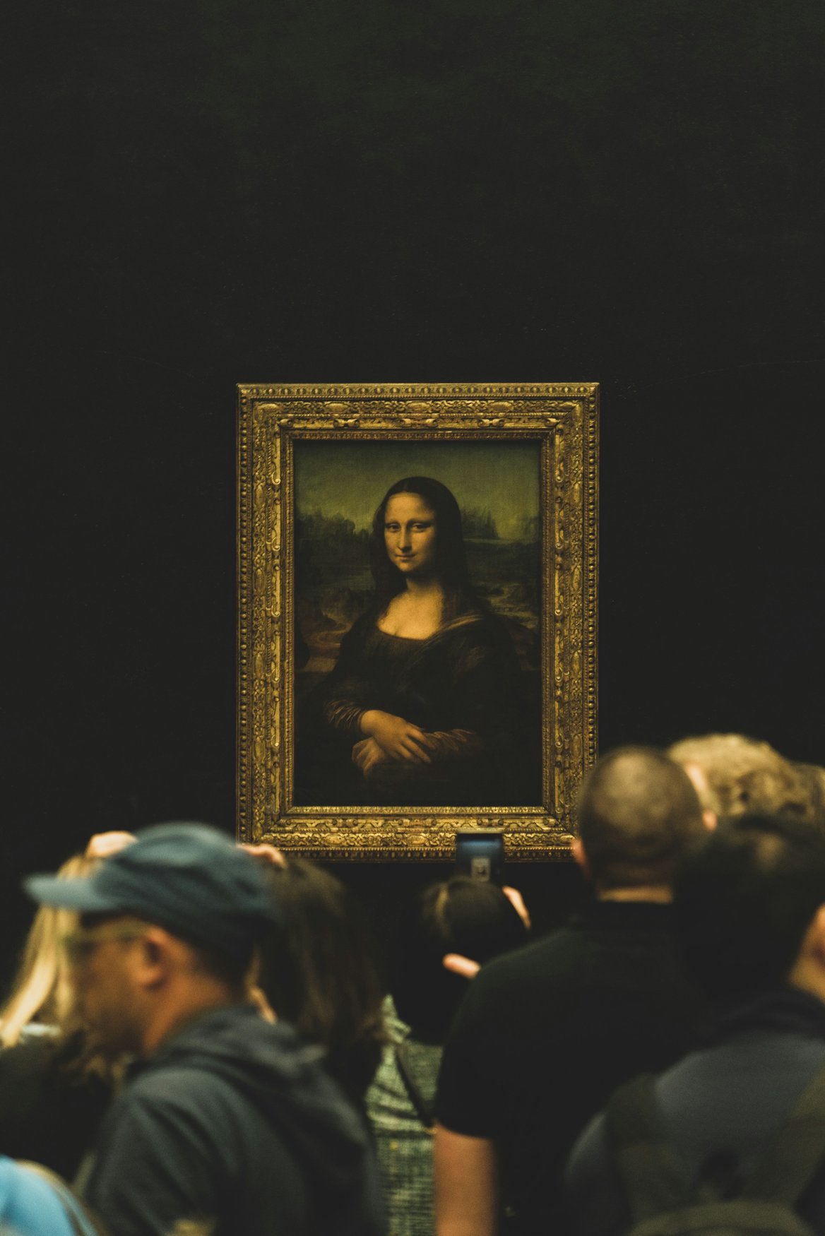 Leonardo da Vincis Mona Lisa im vergoldeten Rahmen an dunkler Wand, davor eine dichte Gruppe von Besuchern.
