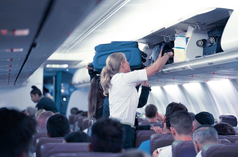 Flugbegleiterin hilft dabei, Koffer im Handgepäckfach zu verstauen