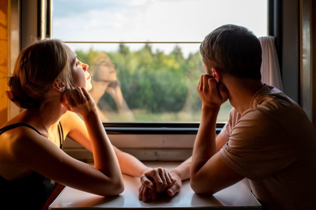 Junges Paar sitzt händchenhaltend im Zug und blickt aus dem Fenster 