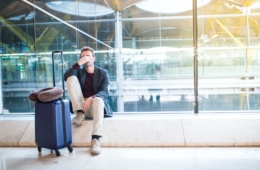 Mann sitzt am Flughafen und ist wegen Reiserücktritt verzweifelt