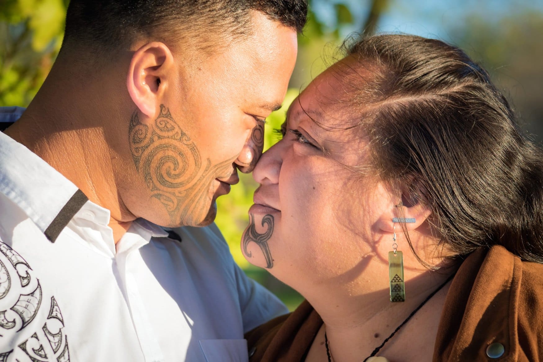 Ein Mann und eine Frau der Māori berühren sich zur Begrüßung mit Nase und Stirn, der sogenannte Hongi. Beide tragen Ta-Moko-Tätowierungen im Gesicht, aufgenommen in Rotorua in Neuseeland.