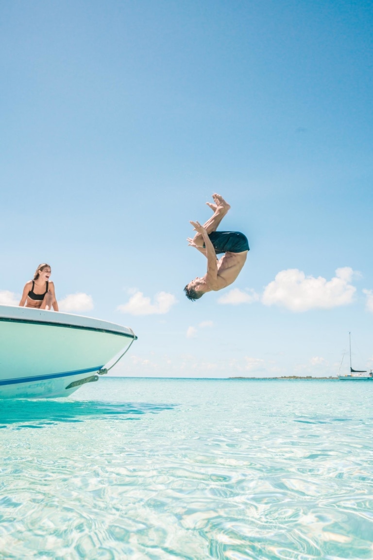 Mann macht Salto von einem Boot ins Meer im Bahamas Urlaub