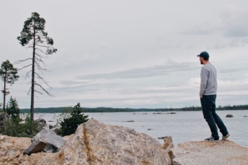 Mann steht an einem See in Finnland und blickt in die Ferne