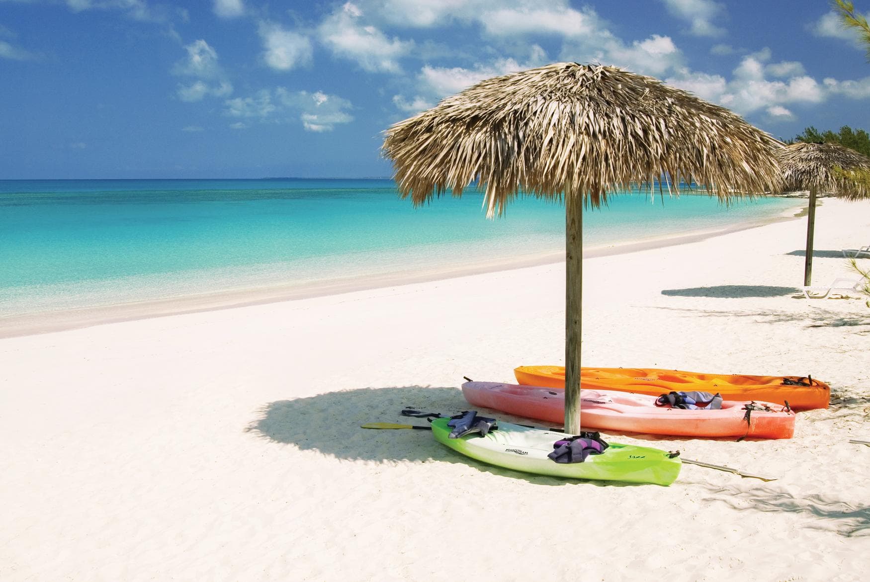 Bunte Kayaks liegen unter Sonnenschirm an Strand von Cat Island