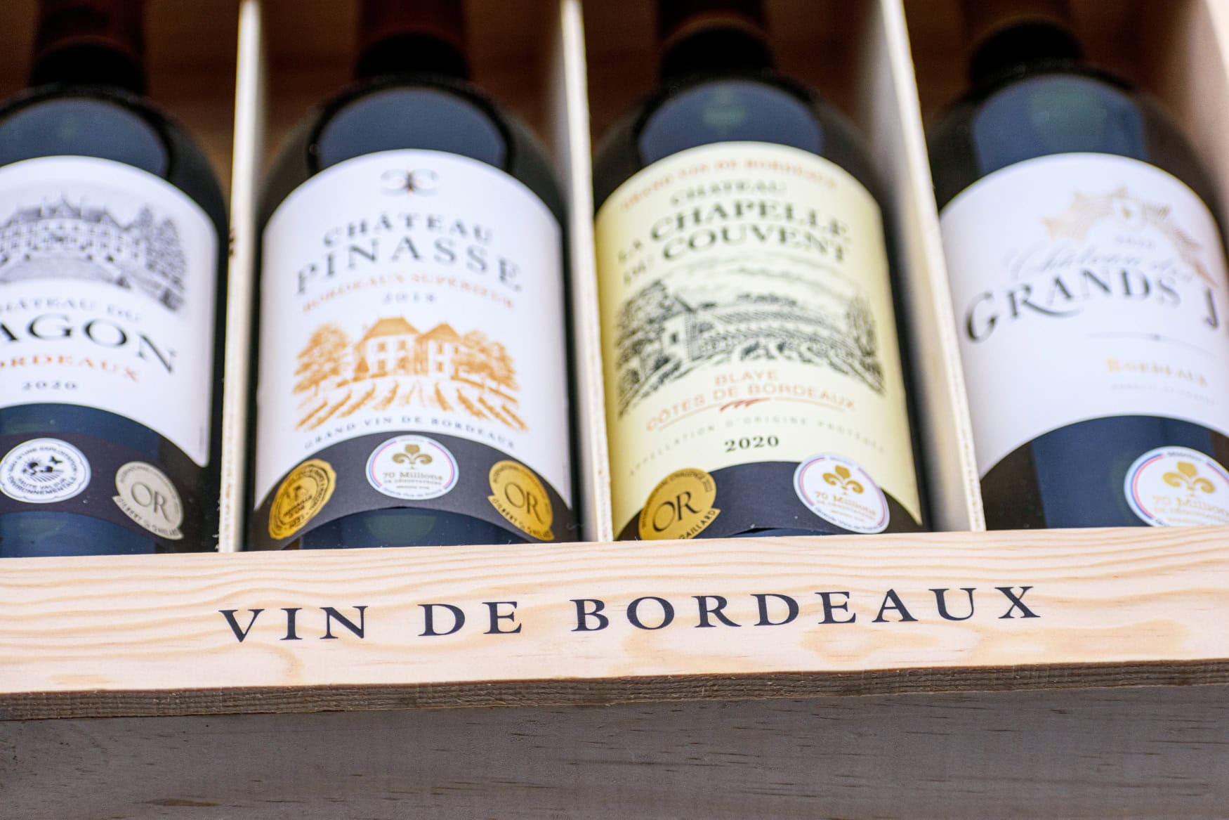 In einer Holzkiste mit der Aufschrift "Vin de Bordeaux" liegen vier Flaschen Rotwein