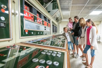 Familie im Regierungsbunker Ahrtal; eine Mädchen zeigt begeistert auf einige Elemente an einer Konsole
