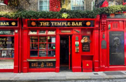 Ein Ziegelgebäude mit rot verkleidetem Erdgeschoss; links ein großes Fenster, rechts eine Tür, darüber die Aufschrift »The Temple Bar«.