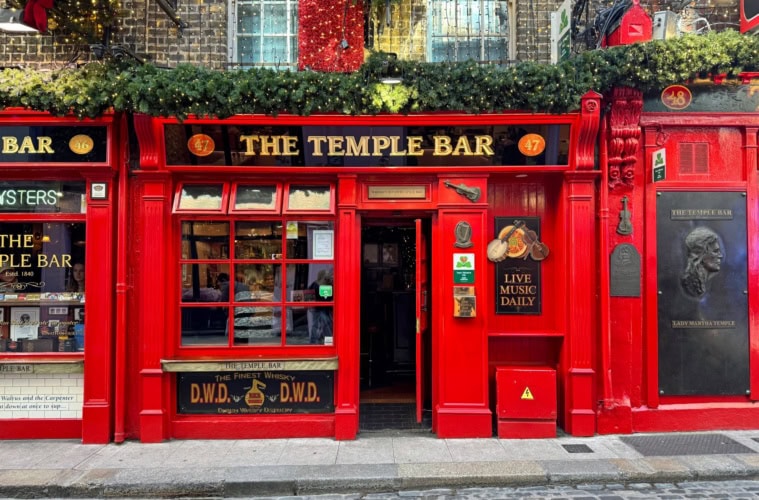 Ein Ziegelgebäude mit rot verkleidetem Erdgeschoss; links ein großes Fenster, rechts eine Tür, darüber die Aufschrift »The Temple Bar«.