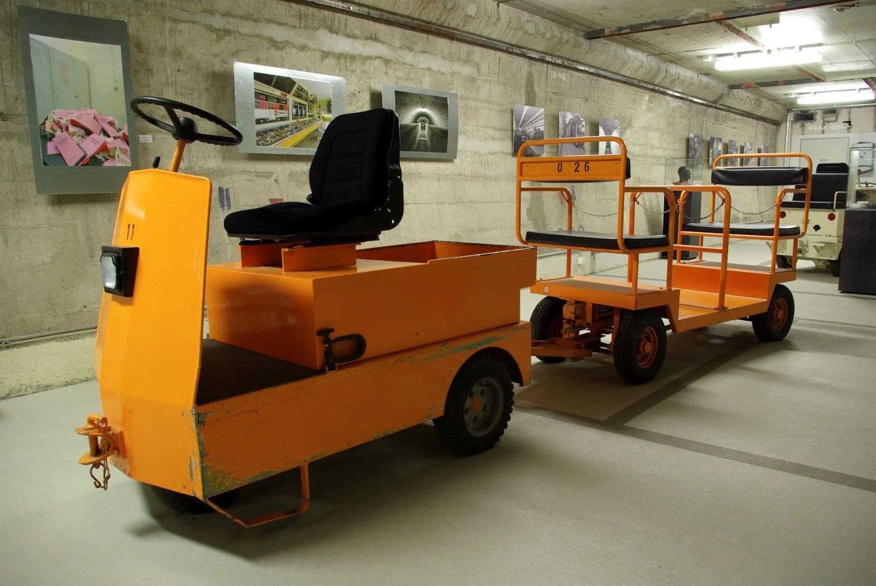 Ein gelbes, kleines Transportfahrzeug in einem Gang des Regierungsbunkers in Ahrweiler. An den Wänden hängen Fotos, die die frühere Einrichtung des Bunkers zeigen
