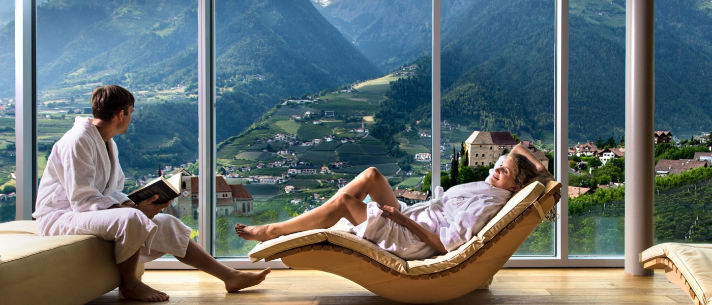Frau und Mann entspannen in Bademänteln in einem Wellnessbereich vor der Kulisse Südtirols