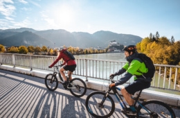 Fahrradfahrer fahren über Brücke in Kufstein mit Blick aufs Schloss