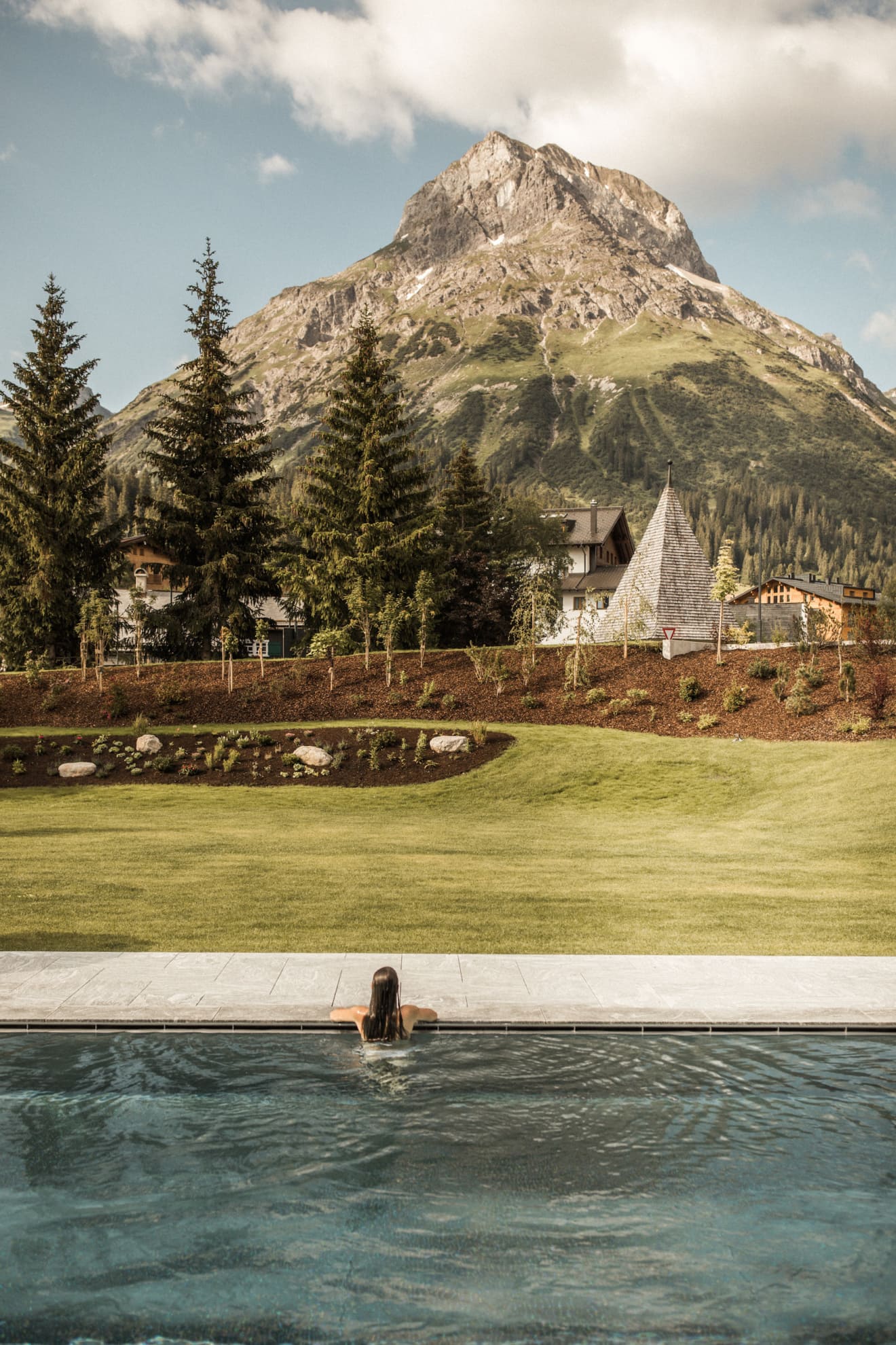 Hotelgast sitzt in Outdoor-Pool und blickt auf die umliegenden Berge im österreichischen Lech