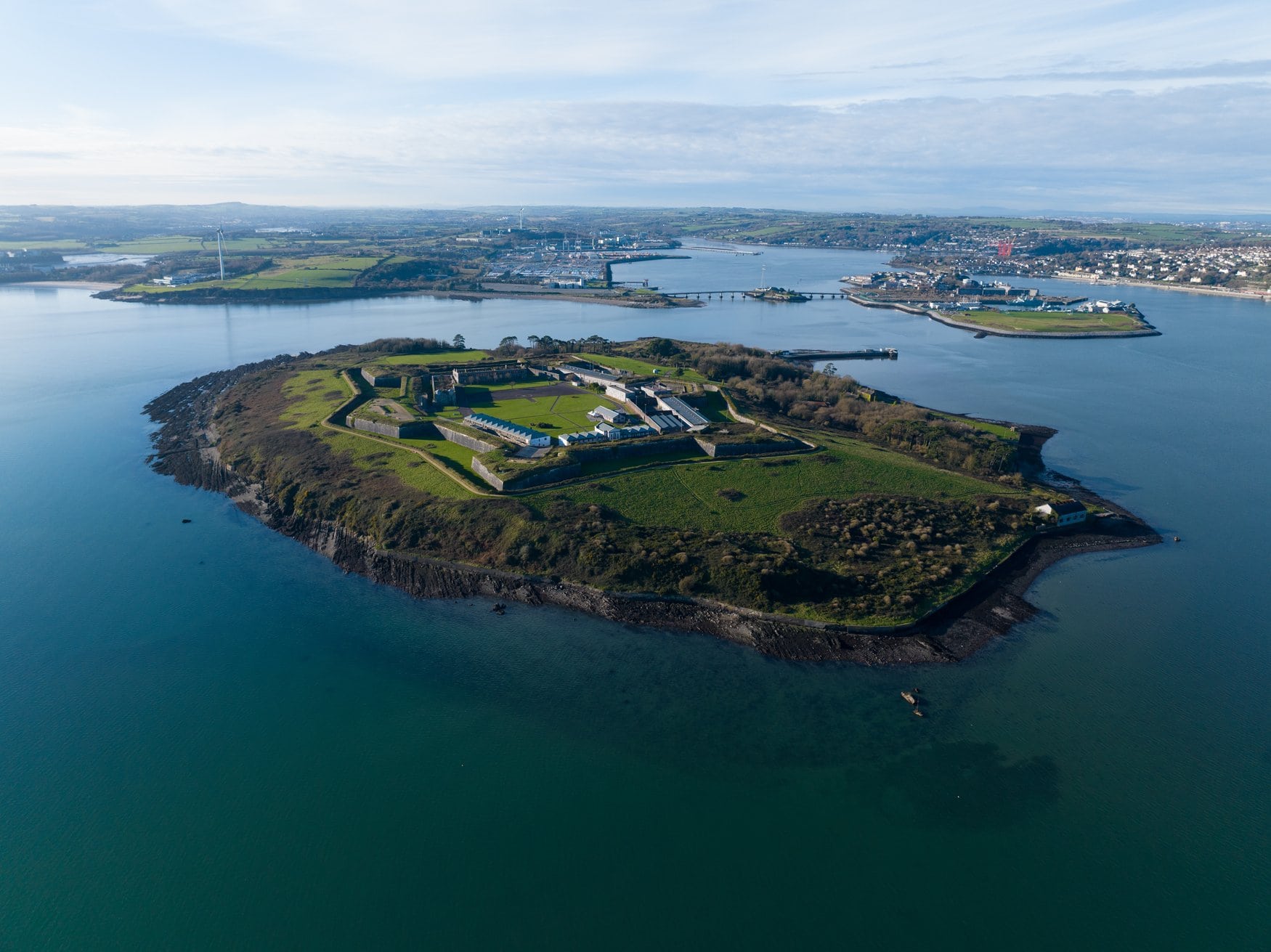 Luftaufnahme von Spike Island im Hafen von Cork mit der sternförmigen Festung, die früher als Gefängnis diente. Rundum liegt die Insel im Wasser, im Hintergrund die grüne Küste.