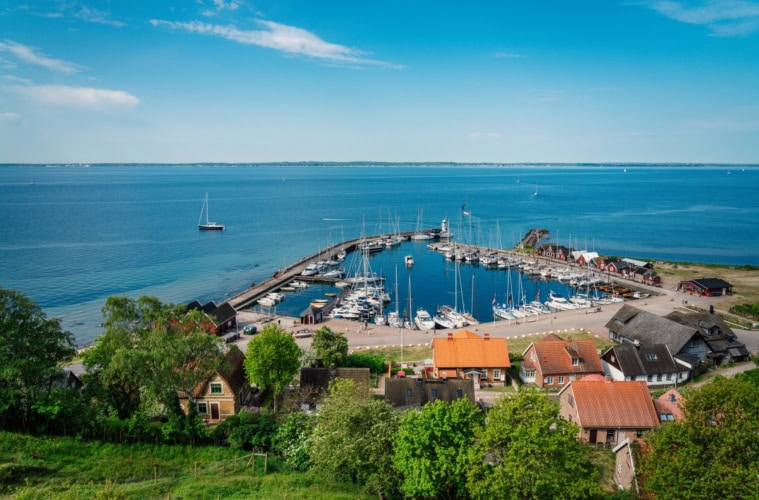 Ausblick von einem grünen Hügel auf einen kleinen Yacht-Hafen auf einer Ostseeinsel. Der Himmel über der Szene ist sommerlich-blau.