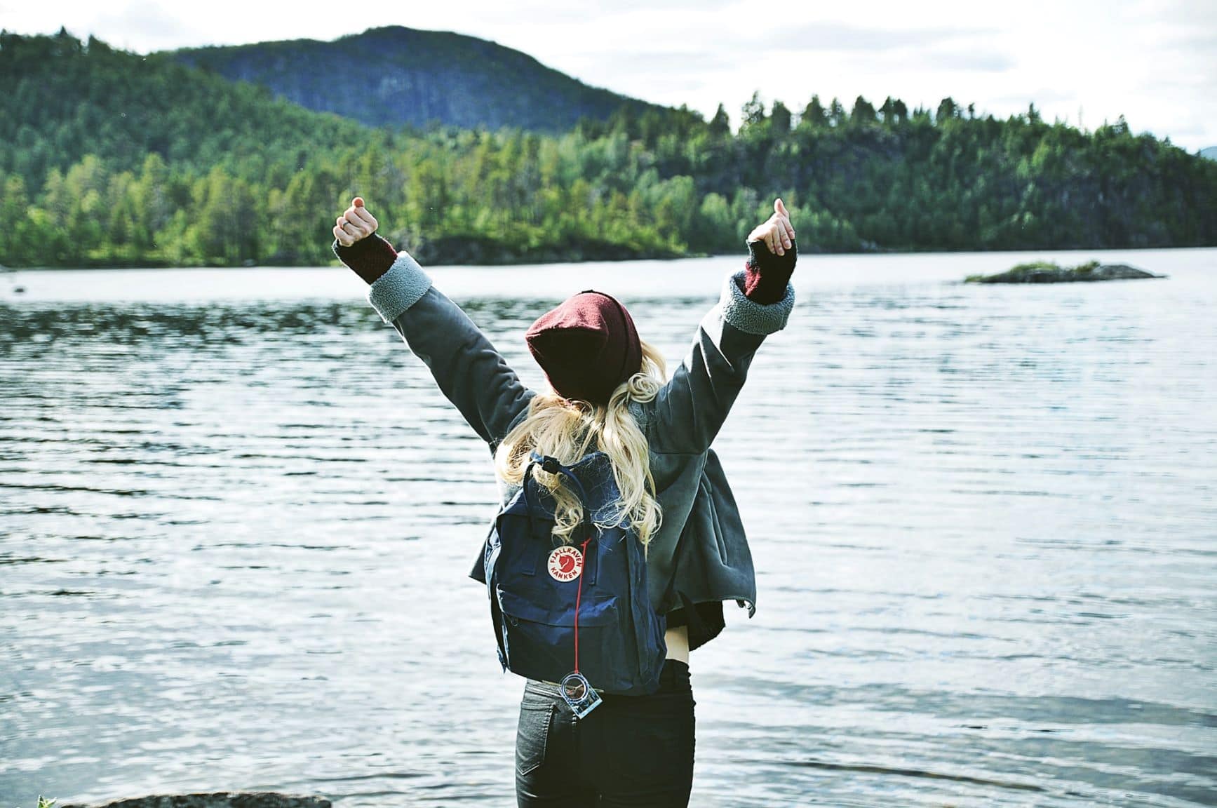 Frau steht vor einem See in Lappland (Schweden) und strecke die Hände in die Höhe