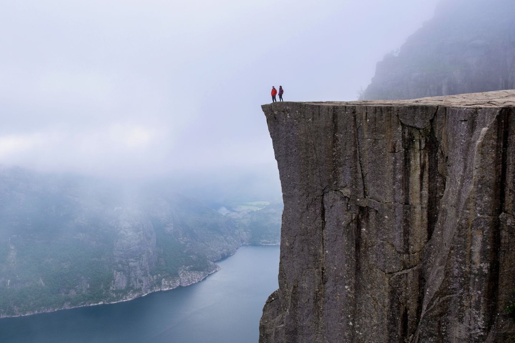 Zwei Personen steht auf dem Plateau Pulpit Rock (Preikestolen) in Norwegen 
