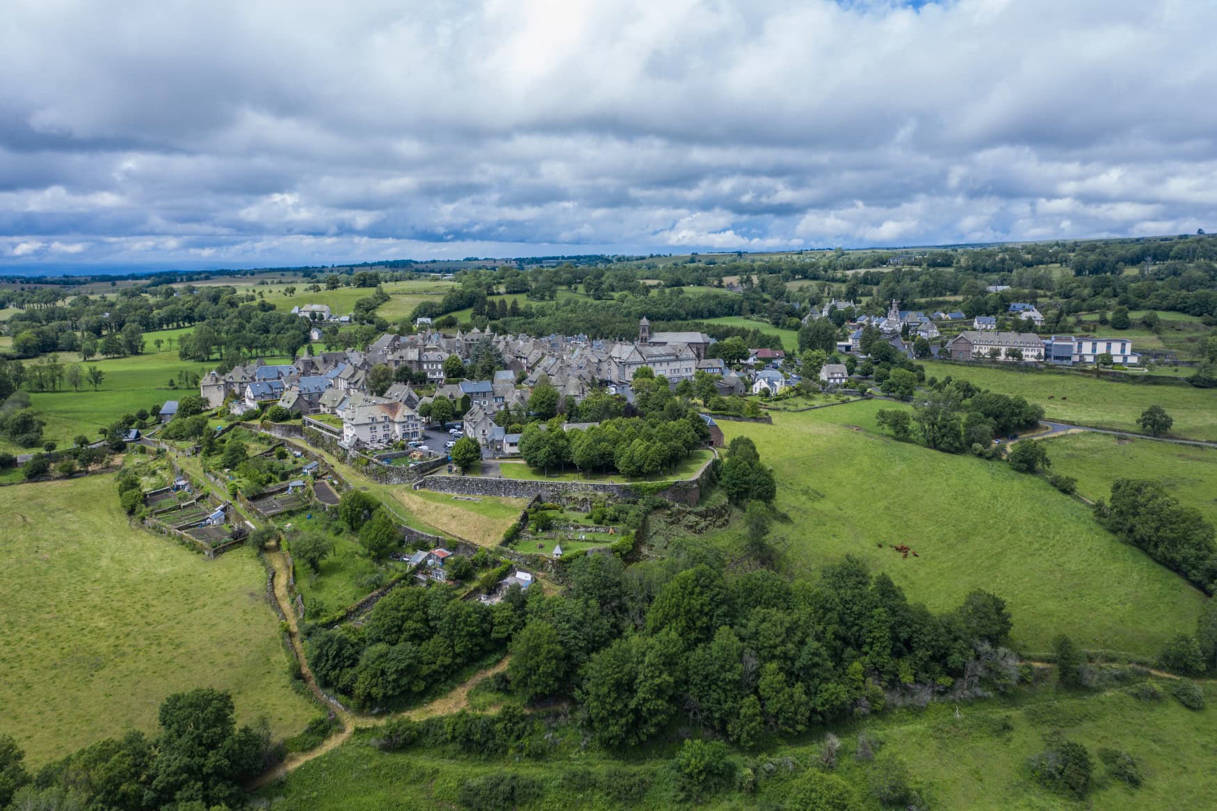 Luftaufnahme des Dorfs Salers in Frankreich, inmitten grüner Wiesen und Wälder