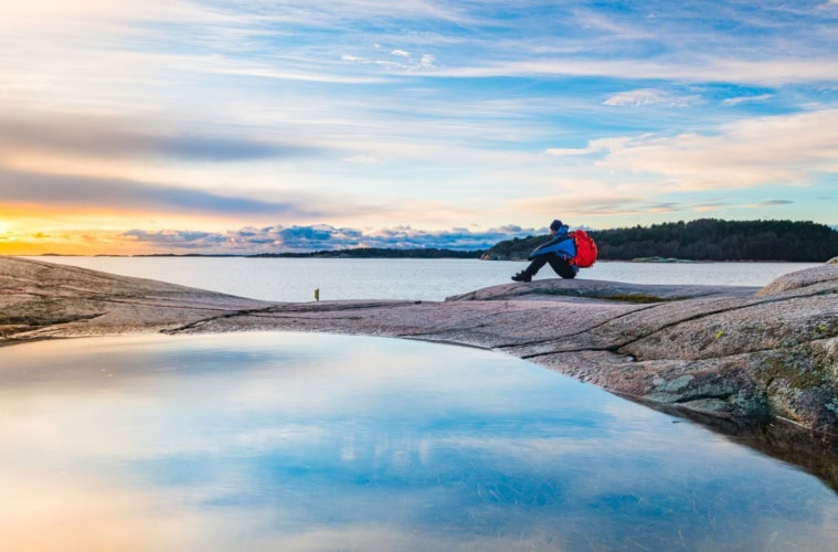 Natururlaub in Schweden: Mann sitzt an Küste auf Felsen und genießt die Aussicht