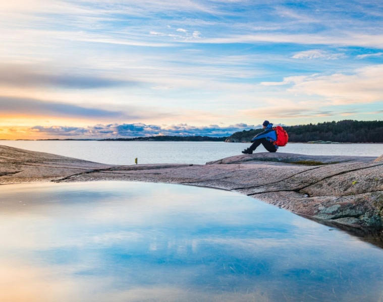 Natururlaub in Schweden: Mann sitzt an Küste auf Felsen und genießt die Aussicht