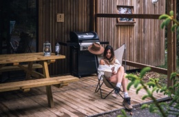 Frau sitzt vor Holzhütte im Wald und liest ein Buch
