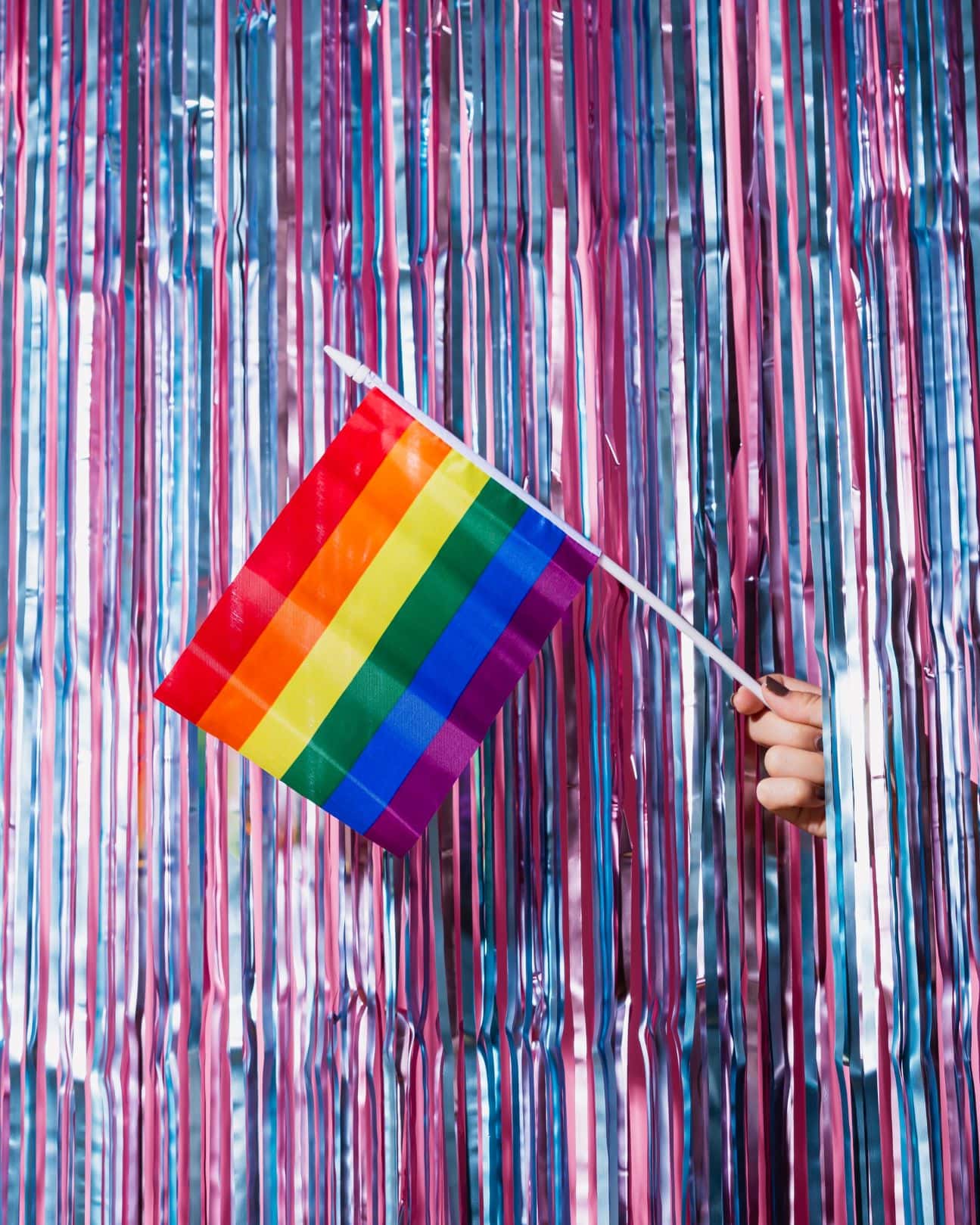 Hand hält ein Regenbogen-Flagge vor Lametta-Vorhang 