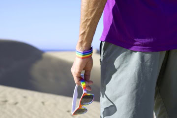 Mann in den Dünen in Maspalomas auf Gran Canaria mit Regenbogen-Accessoires