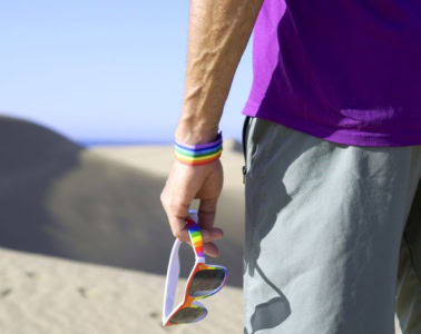 Mann in den Dünen in Maspalomas auf Gran Canaria mit Regenbogen-Accessoires