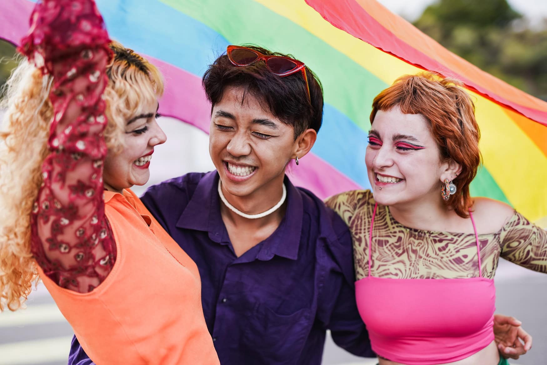 Drei junge Menschen mit eine Pride Flag im Hintergrund