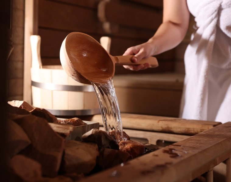 Mensch giesst in der Sauna Wasser auf heiße Steine