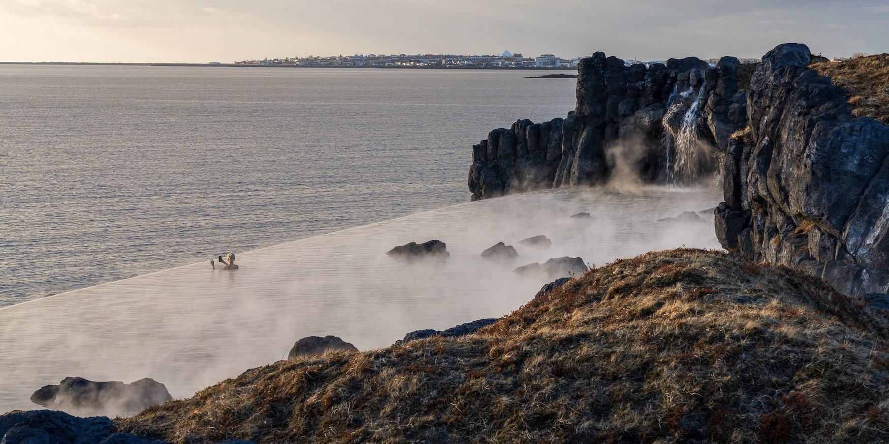 Frau schwimmt in infinity Pool vor der Kulisse der isländischen Hauptstadt Reykjavik
