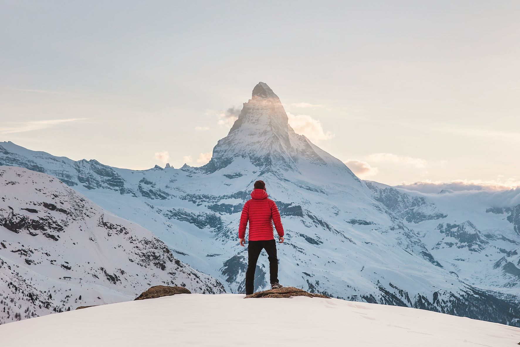 Junger Mann steht in Alpen vor Bergkulisse im Winter 