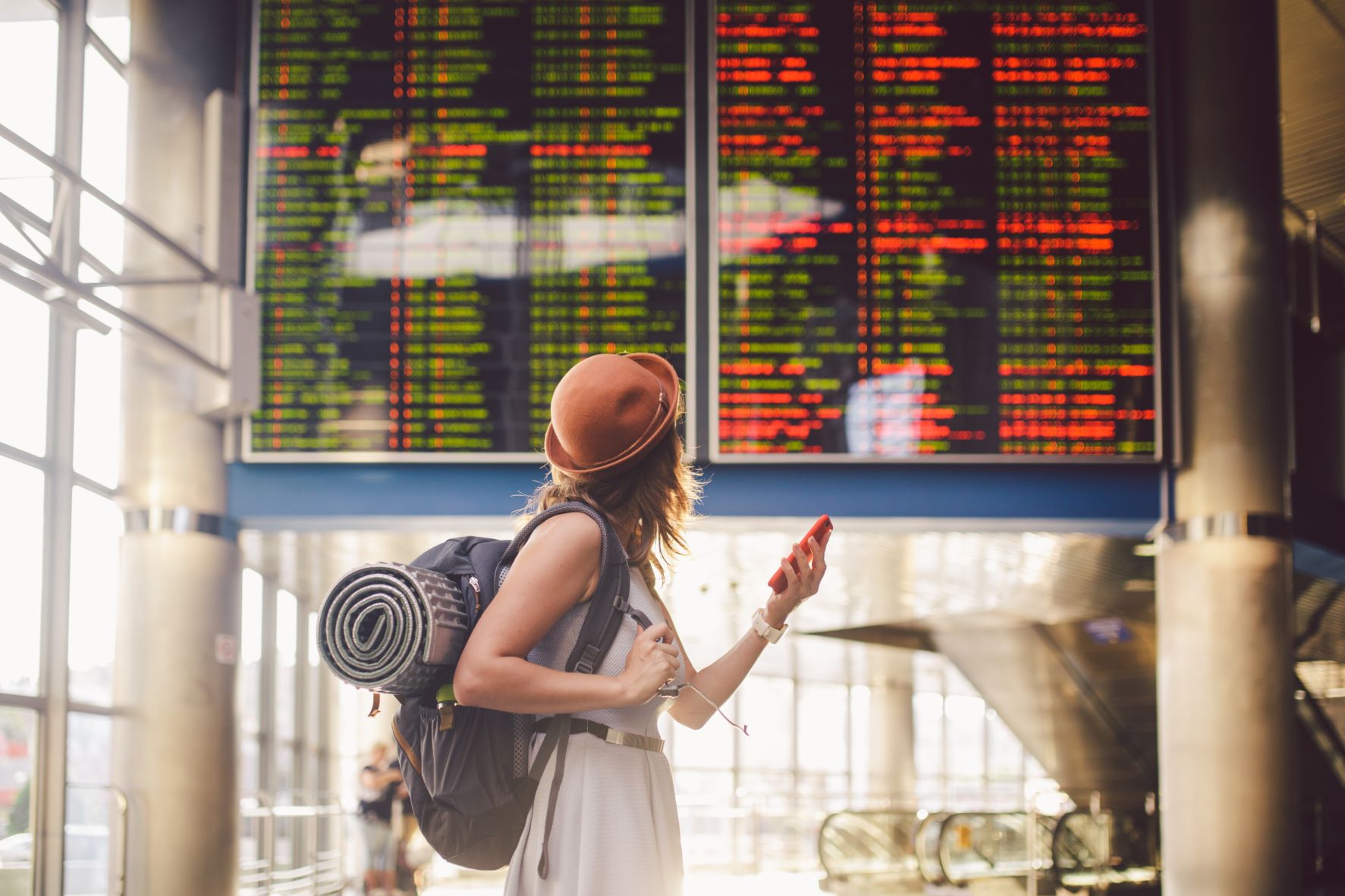 Junge Frau im Flughafen blickt auf große Abflug-Anzeigetafel 