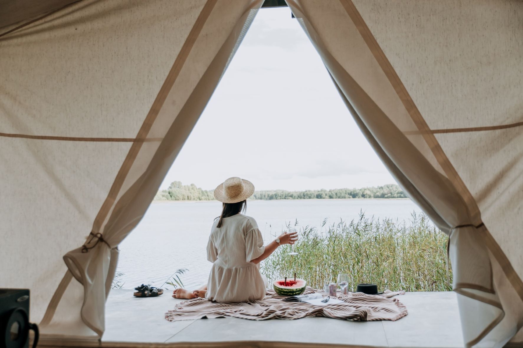 Junge Frau picknickt vor Glamping-Zelt und blickt auf See