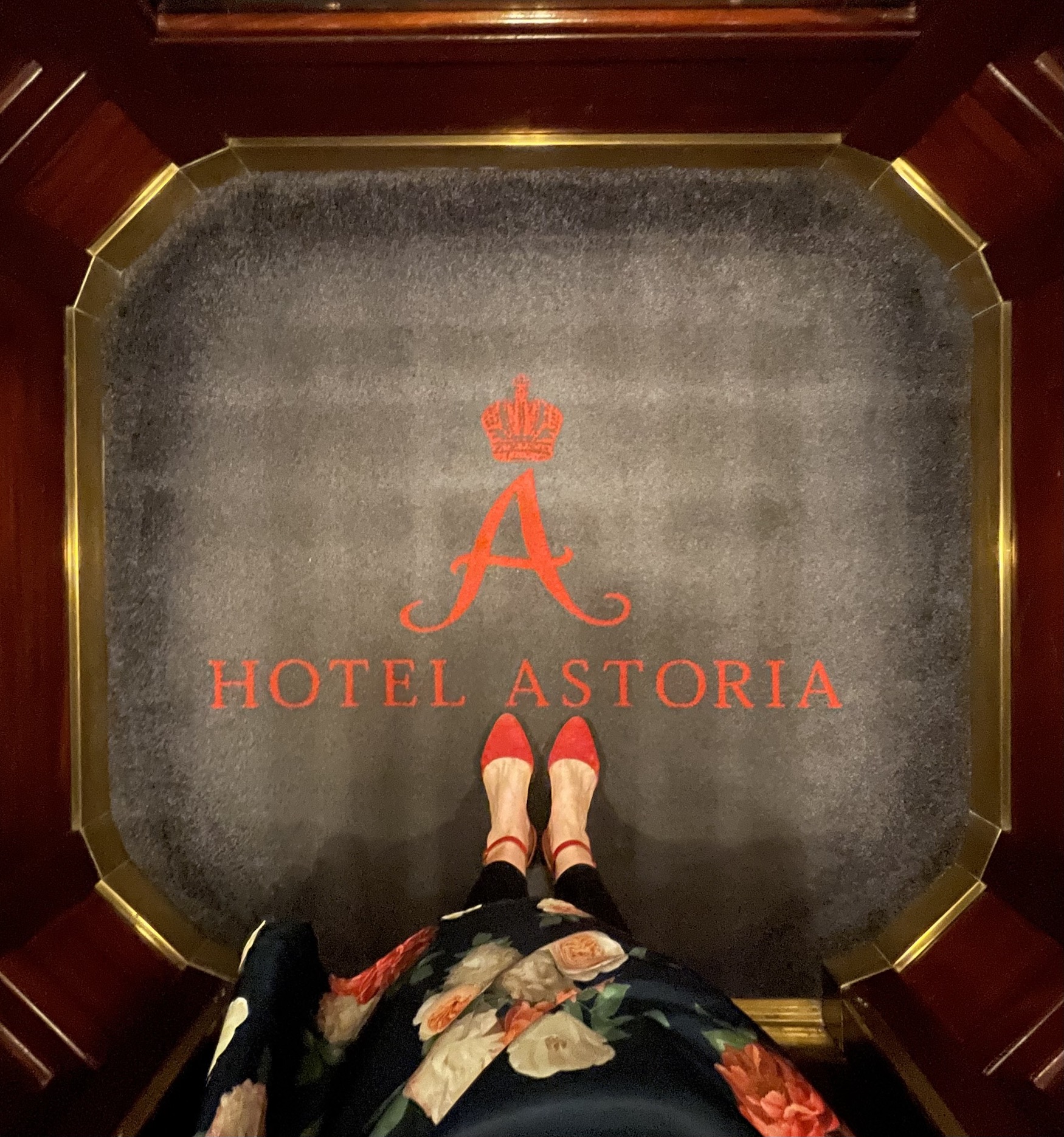 Rote Schuhe auf Hotelteppich mit der Aufschrift: Hotel Astoria