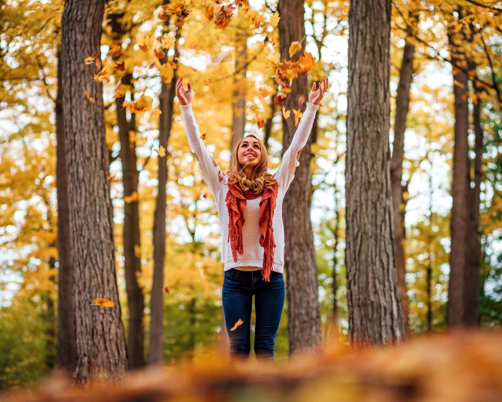 Junge Frau im Wald, wirft Herbst-Blätter in die Höhe