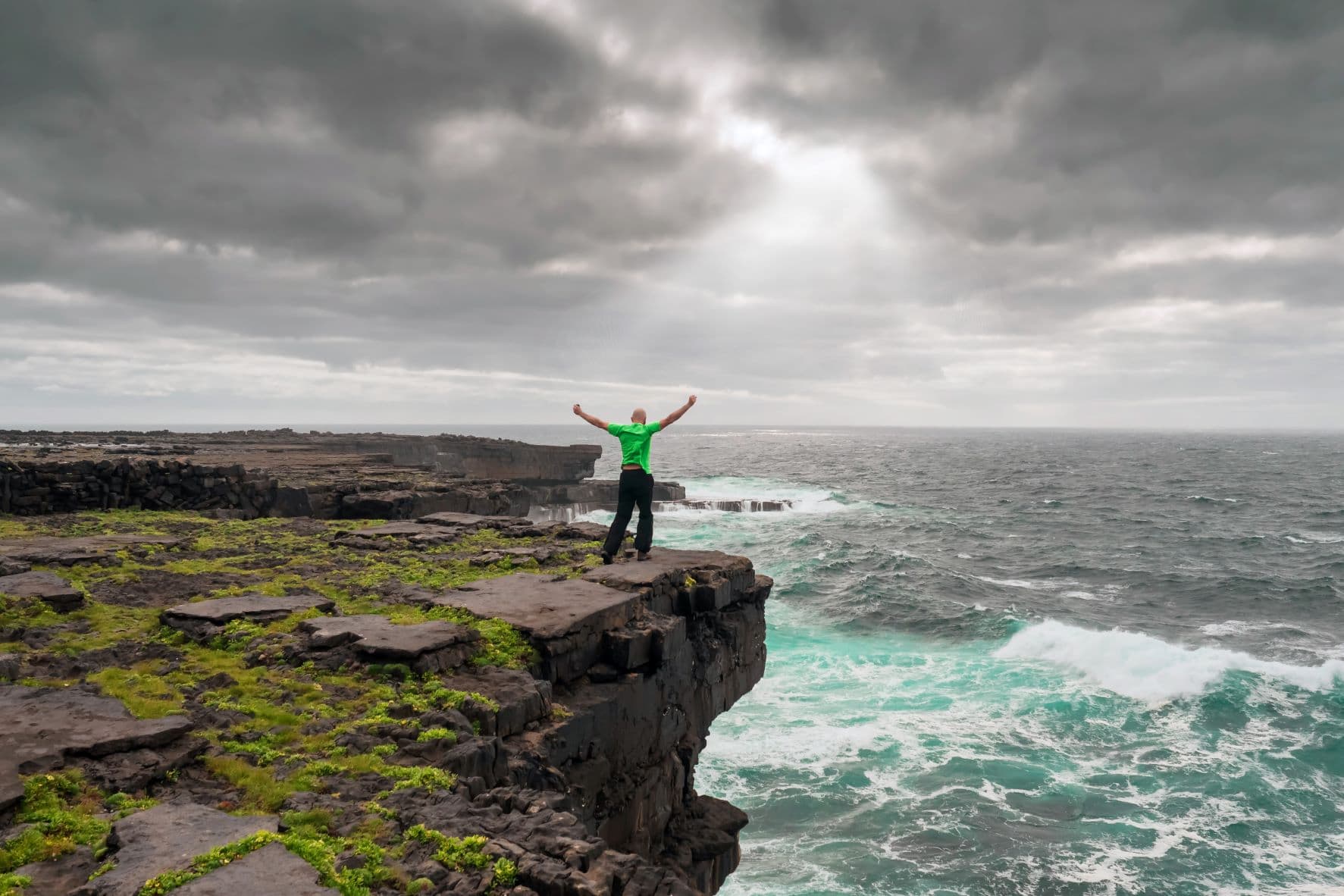 Mann in grünem T-Shirt an einer Klippe an der irischen Küste