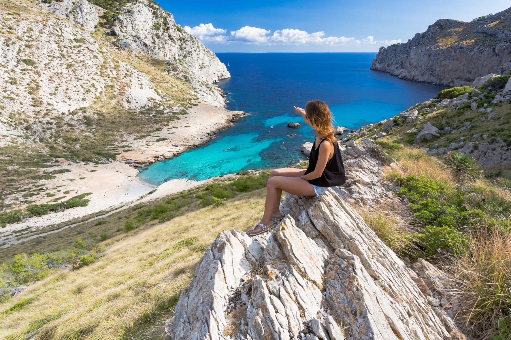 Junge Frau sitzt auf Felsen und blickt auf Bucht auf Formentera 