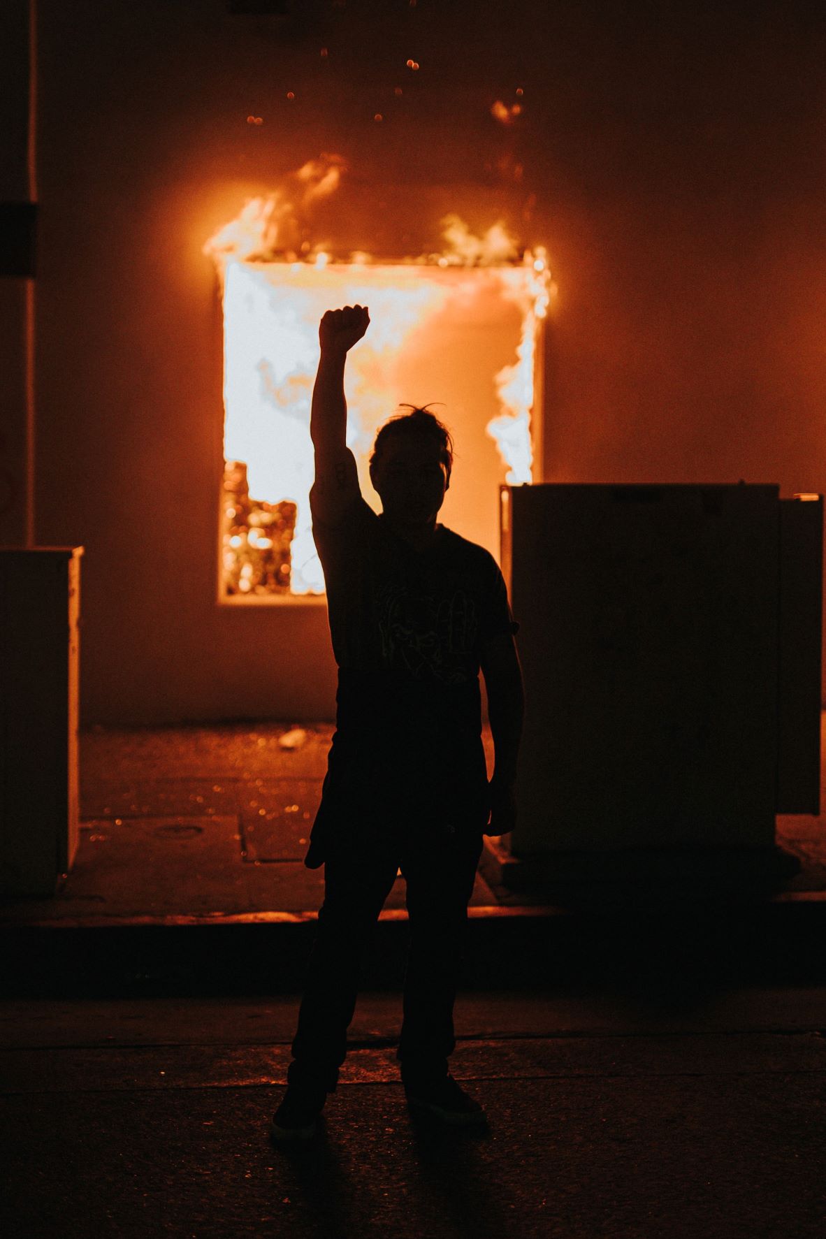 Demonstrant hebt die rechte Hand, im Hintergrund Feuer 